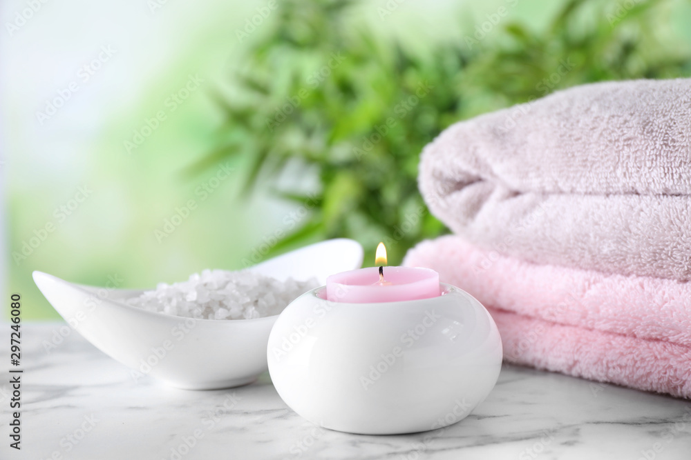 Composition with sea salt, candle and towels on white marble table against blurred background. Spa concept Composition with sea salt, candle and towels on white marble table against blurred background. Spa concept