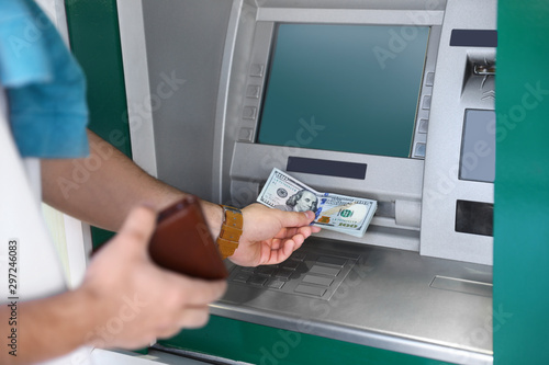 Young man taking money from cash machine outdoors, closeup