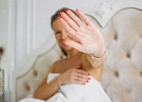 Happy smiling beautiful long hair young woman pulling hand towards camera sitting on bed, selective focus on hand