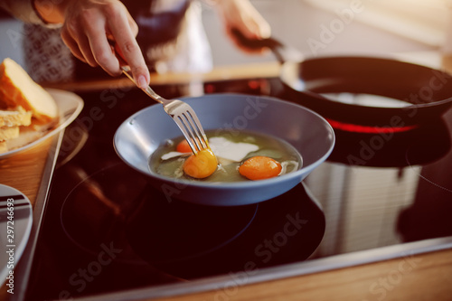 Close up of caucasian woman in apron standing next to stove and preparing sunny side up eggs for breakfast.