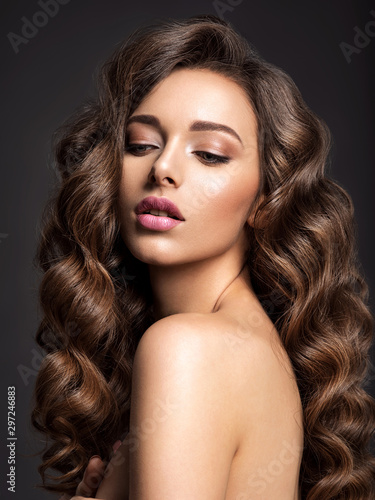 Beautiful woman with long brown hair. Beautiful face of an attractive model with natural makeup. Beauty of curly hair. Closeup portrait of caucasian stunning girl.