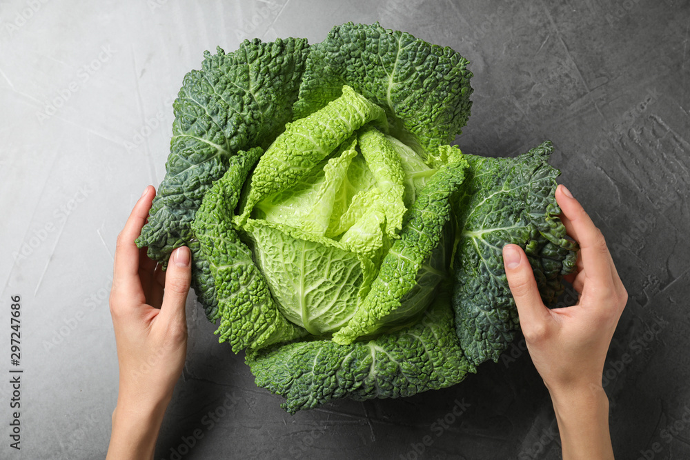 Woman with fresh green savoy cabbage at grey table, top view - obrazy, fototapety, plakaty 