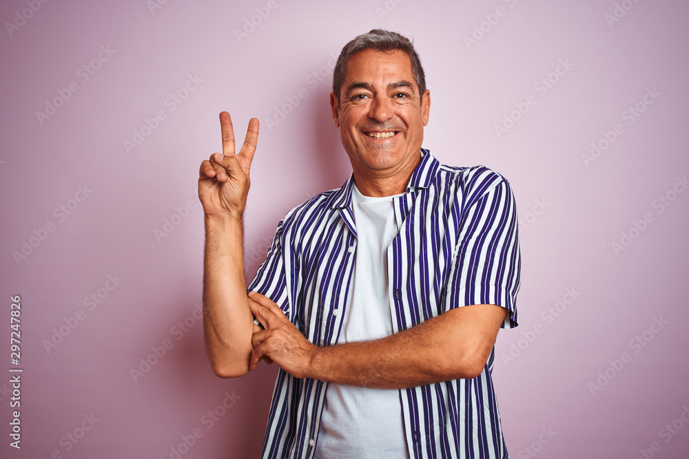 Handsome middle age man wearing striped shirt standing over isolated pink background smiling with happy face winking at the camera doing victory sign. Number two. Handsome middle age man wearing striped shirt standing over isolated pink background smiling with happy face winking at the camera doing victory sign. Number two.