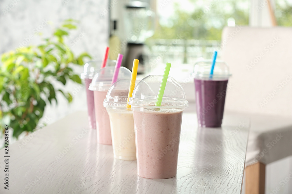 Different milk shakes in plastic cups on white wooden table indoors Different milk shakes in plastic cups on white wooden table indoors