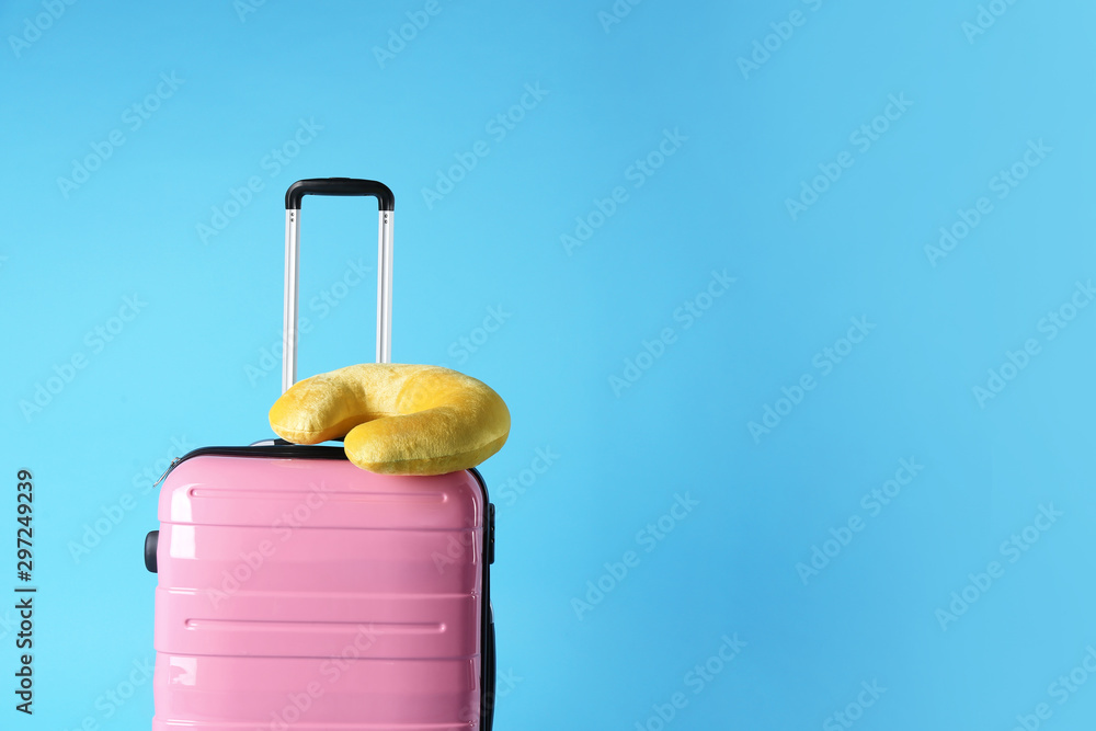 Pink suitcase and travel pillow on light blue background, space for text