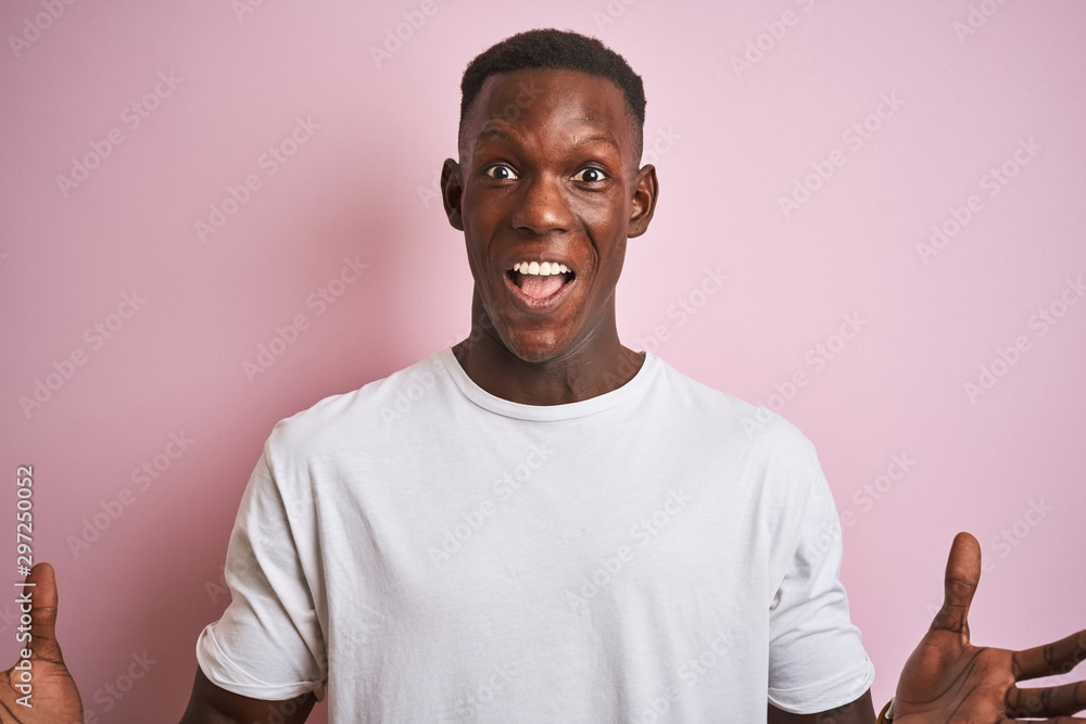 African american man wearing white t-shirt standing over isolated pink background very happy and excited, winner expression celebrating victory screaming with big smile and raised hands African american man wearing white t-shirt standing over isolated pink background very happy and excited, winner expression celebrating victory screaming with big smile and raised hands