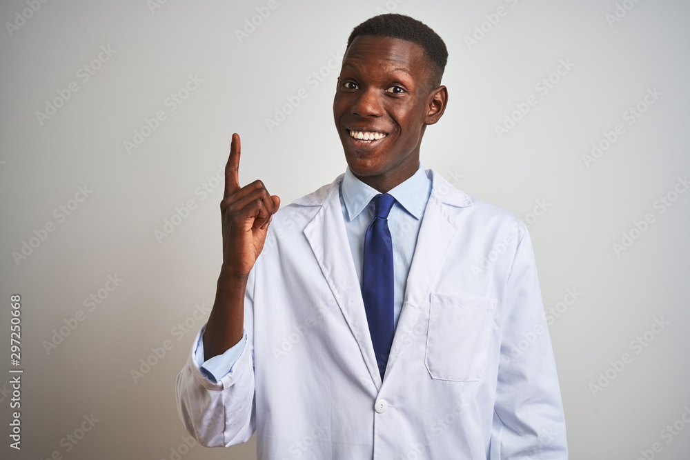 Young african american doctor man wearing coat standing over isolated white background pointing finger up with successful idea. Exited and happy. Number one. Young african american doctor man wearing coat standing over isolated white background pointing finger up with successful idea. Exited and happy. Number one.
