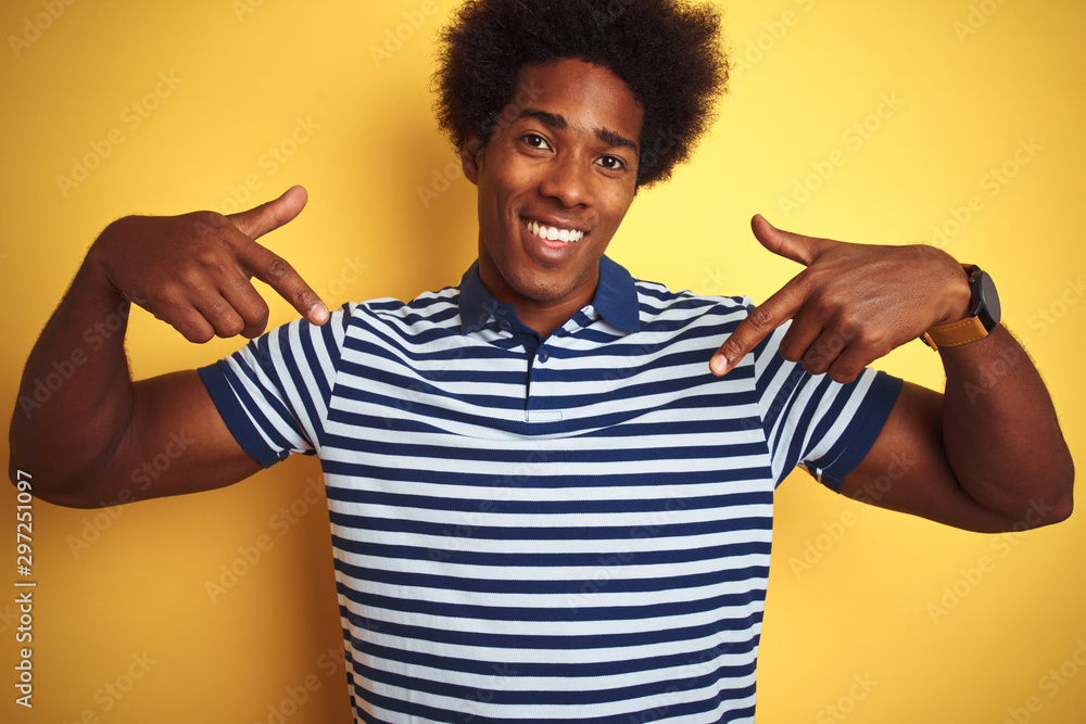 American man with afro hair wearing navy striped polo standing over isolated yellow background looking confident with smile on face, pointing oneself with fingers proud and happy. American man with afro hair wearing navy striped polo standing over isolated yellow background looking confident with smile on face, pointing oneself with fingers proud and happy.