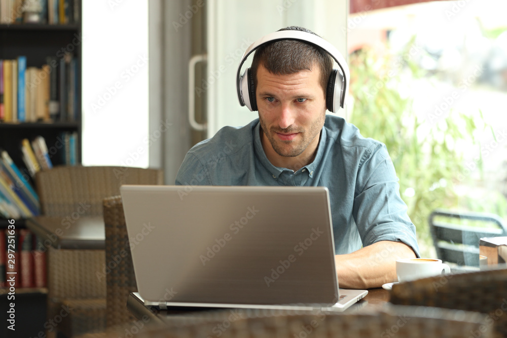 Serious man using a laptop with headphones in a bar Serious man using a laptop with headphones in a bar