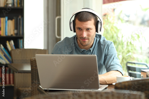 Serious man using a laptop with headphones in a bar