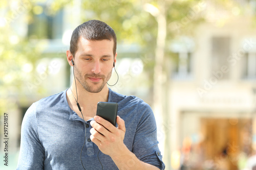 Adult man listening to music checking cell walking in the street