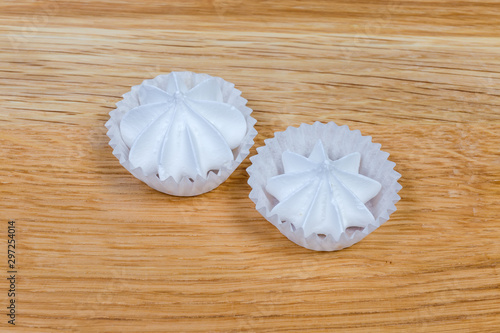 Meringue cookies in ruffled paper molds on the wooden surface