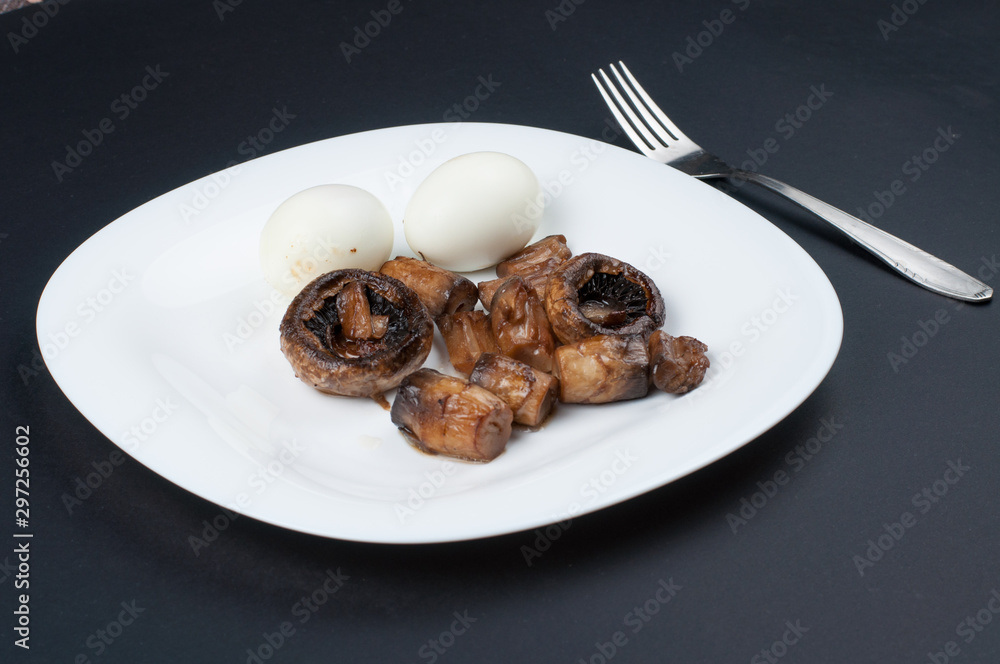 Mushrooms and boiled eggs on a white plate isolated on a black background.Natural food Mushrooms and boiled eggs on a white plate isolated on a black background.Natural food
