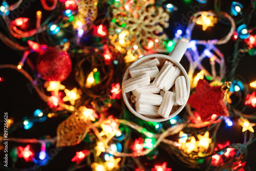 Cup of homemade hot chocolate with white marshmallows, a lot of lights of stars garland and christmas tree ornament, christmas and new year concept