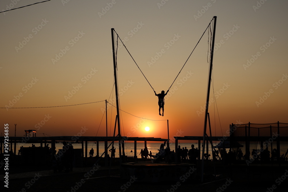 Trampoline jumping with ropes during sunset at the Black Sea in Anapa, Russia. Trampoline jumping with ropes during sunset at the Black Sea in Anapa, Russia.