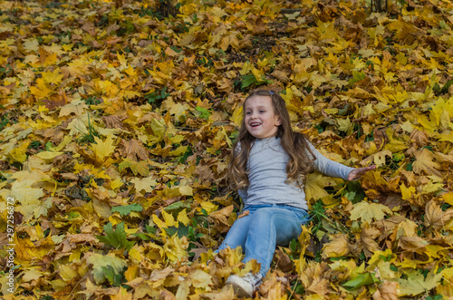 Little charming girl child throws up fallen yellow maple leaves in autumn park