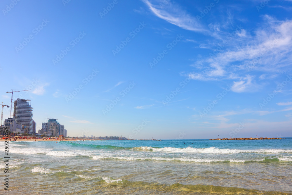 Gorgeous calm blue sea and Tel Aviv free sand beaches. People enjoy autumn mild season. They sunbathe and swim. Coastal hotels and Old Jaffa fortress on horizon