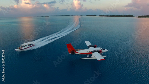 Aerial photo of seaplane during sunset. White black red seaplane docked in the middle of the Maldivian lagoon of Indian Ocean, far away from Island. Speed boat is passing by photo