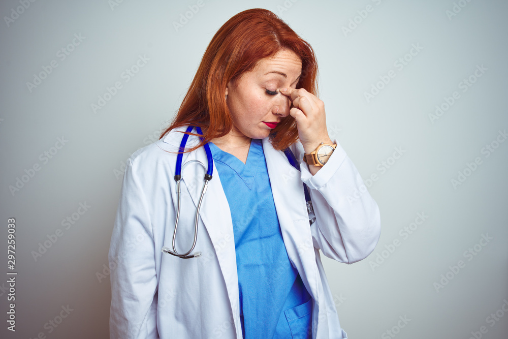 Young redhead doctor woman using stethoscope over white isolated background tired rubbing nose and eyes feeling fatigue and headache. Stress and frustration concept. Young redhead doctor woman using stethoscope over white isolated background tired rubbing nose and eyes feeling fatigue and headache. Stress and frustration concept.