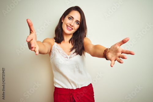 Young beautiful woman wearing t-shirt standing over white isolated background looking at the camera smiling with open arms for hug. Cheerful expression embracing happiness.