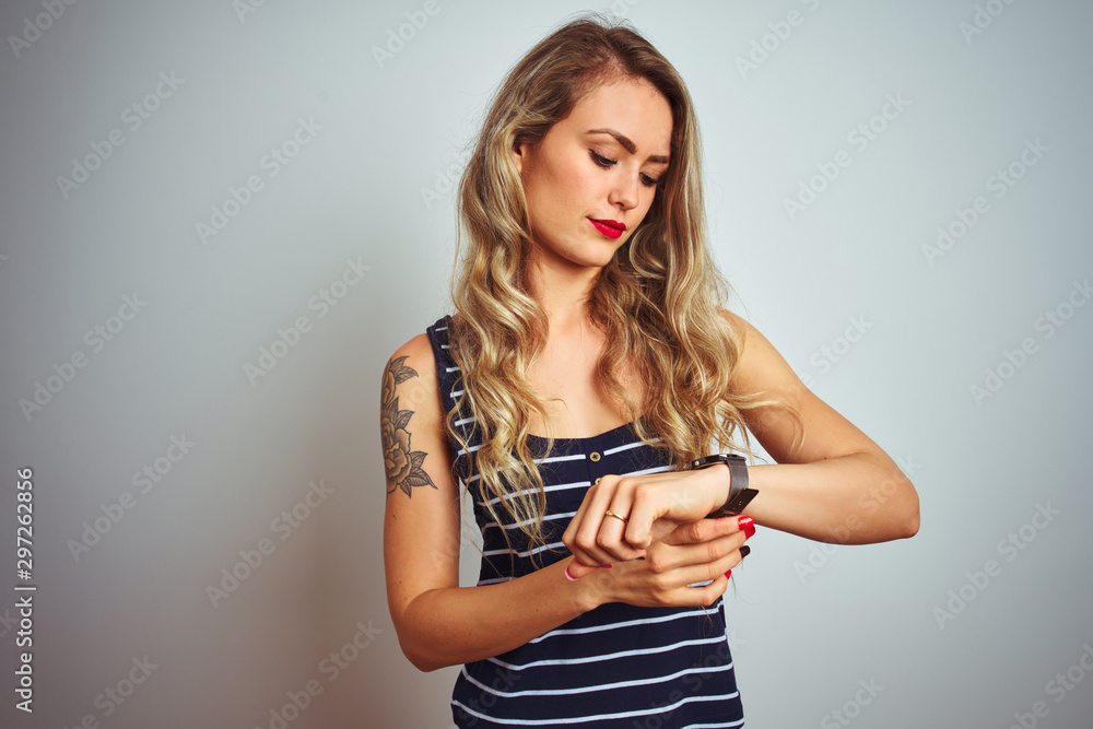 Young beautiful woman wearing stripes t-shirt standing over white isolated background Checking the time on wrist watch, relaxed and confident Young beautiful woman wearing stripes t-shirt standing over white isolated background Checking the time on wrist watch, relaxed and confident