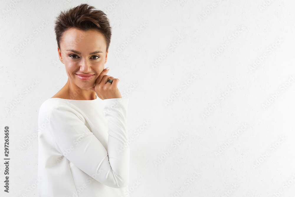 A young beautiful girl with short dark hair, makeup, in a long white dress with her back open, in pink boat shoes stands with her back to the white wall A young beautiful girl with short dark hair, makeup, in a long white dress with her back open, in pink boat shoes stands with her back to the white wall