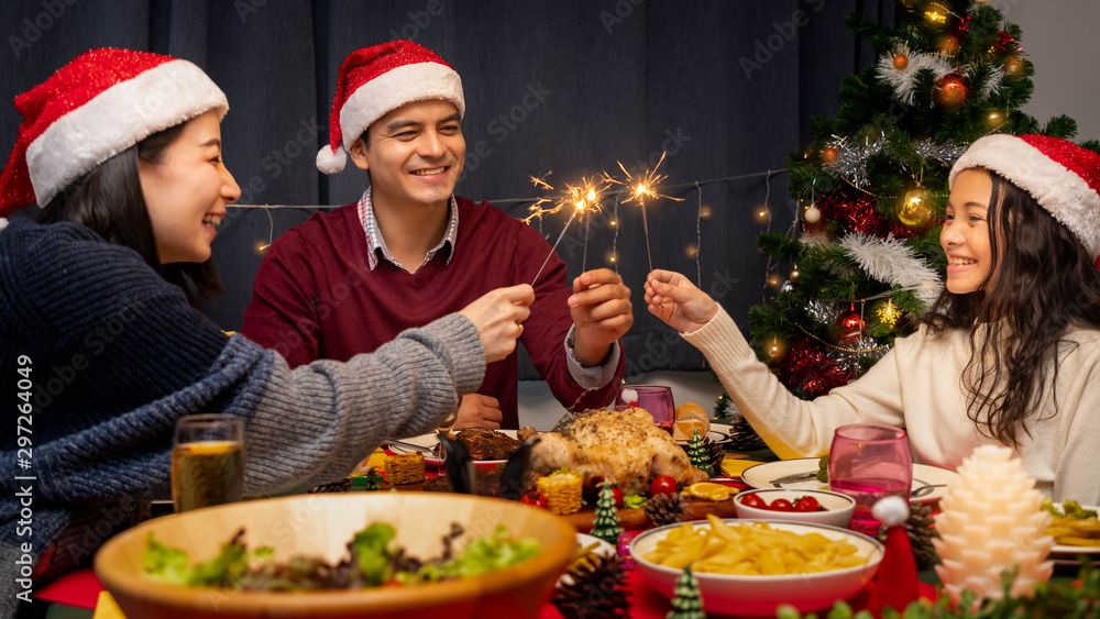 Happy family, father mother and daughter, having dinner together to celebrate Christmas holiday together, with sparkler light Happy family, father mother and daughter, having dinner together to celebrate Christmas holiday together, with sparkler light