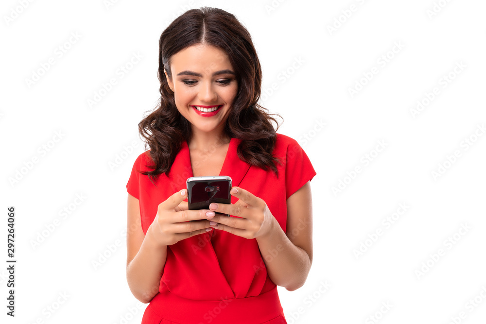 A young woman with red lips, bright makeup, a dazzling smile, dark wavy long hair, in a red summer dress stands with a phone in hand A young woman with red lips, bright makeup, a dazzling smile, dark wavy long hair, in a red summer dress stands with a phone in hand