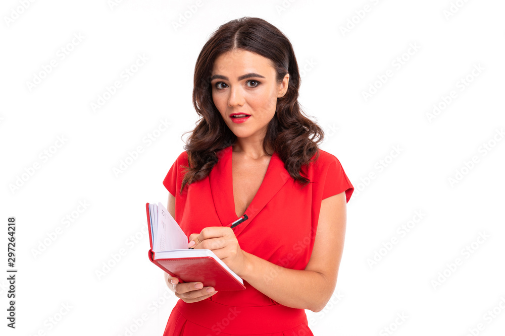 A young woman with red lips, bright makeup, a dazzling smile, dark wavy long hair, in a red summer dress stands and records in a notebook A young woman with red lips, bright makeup, a dazzling smile, dark wavy long hair, in a red summer dress stands and records in a notebook
