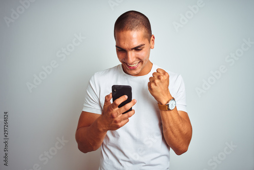 Young handsome man using smartphone over yellow isolated background screaming proud and celebrating victory and success very excited, cheering emotion