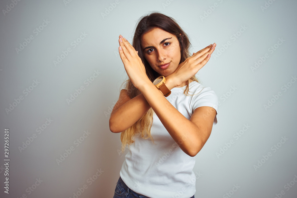 Young beautiful woman wearing casual white t-shirt over isolated background Rejection expression crossing arms doing negative sign, angry face Young beautiful woman wearing casual white t-shirt over isolated background Rejection expression crossing arms doing negative sign, angry face