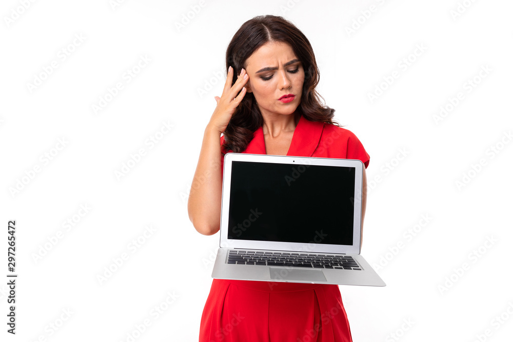 The young woman is red lips, bright makeup, dark wavy long hair, in a red suit, standing with a white laptop and thinking The young woman is red lips, bright makeup, dark wavy long hair, in a red suit, standing with a white laptop and thinking