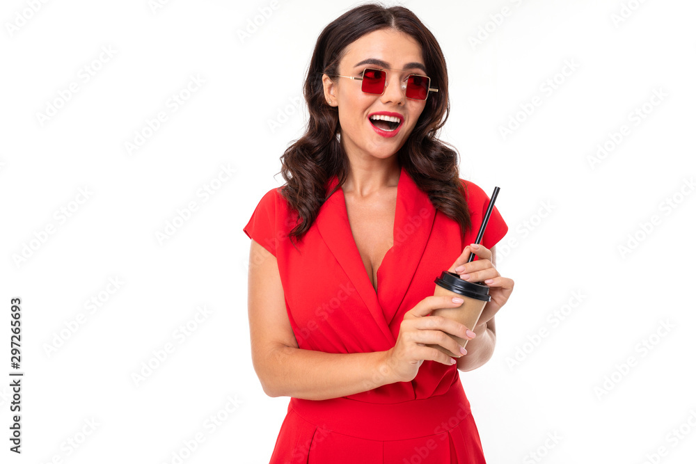 Naklejka premium The young woman is red lips, bright makeup, dark wavy long hair, in a red suit, with red square glasses and a cup of coffee with a tube