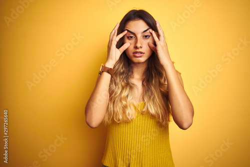 Young beautiful woman wearing t-shirt over yellow isolated background Trying to open eyes with fingers, sleepy and tired for morning fatigue