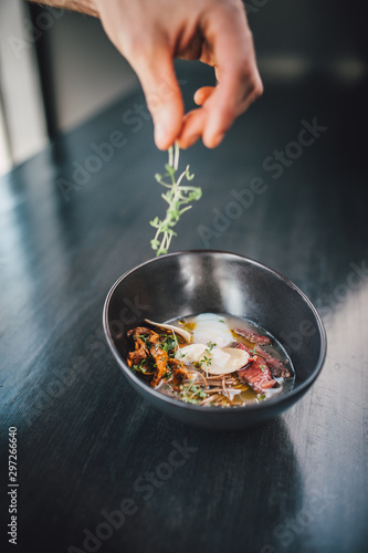 Chef making Miso Ramen Asian noodles with egg, enoki and pak choi cabbage in bowl on dark wooden background background