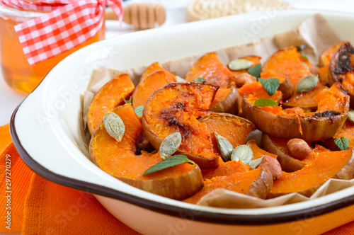 Pumpkin slices baked in the oven with honey, nuts, cinnamon, seeds, mint. Pieces of pumpkin lying on the baking paper in a bowl. Healthy food, dessert for gourmets. Traditional autumn snack