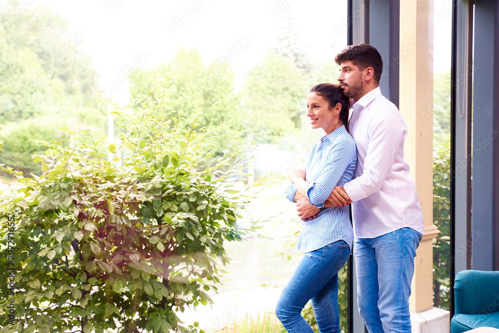 Shot of beautiful young couple standing in living room and looking out the window Shot of beautiful young couple standing in living room and looking out the window