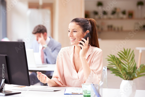 Happy businesswoman giving a call and working on computer in the office