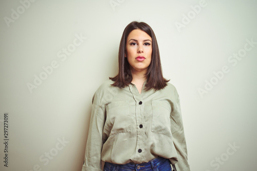 Young beautiful brunette woman wearing green shirt over isolated background with serious expression on face. Simple and natural looking at the camera.