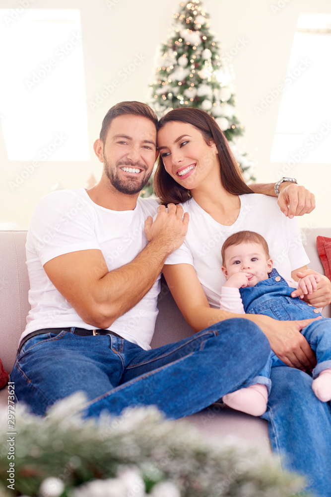 Lovely family with their baby girl relaxing on sofa at home during Christmas Lovely family with their baby girl relaxing on sofa at home during Christmas