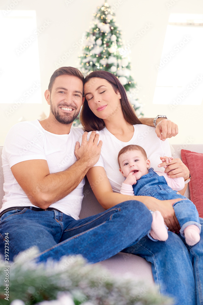 Lovely family with their baby girl relaxing on sofa at home during Christmas Lovely family with their baby girl relaxing on sofa at home during Christmas