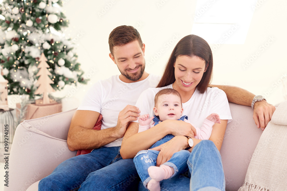 Lovely family with their baby girl relaxing on sofa at home during Christmas Lovely family with their baby girl relaxing on sofa at home during Christmas