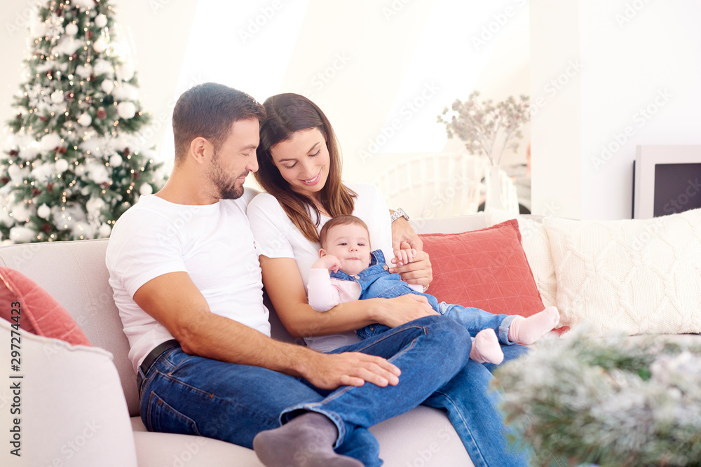 Lovely family with their baby girl relaxing on sofa at home during Christmas Lovely family with their baby girl relaxing on sofa at home during Christmas