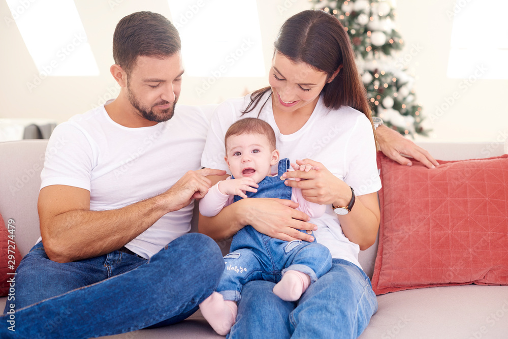 Lovely family with their baby girl relaxing on sofa at home during Christmas Lovely family with their baby girl relaxing on sofa at home during Christmas