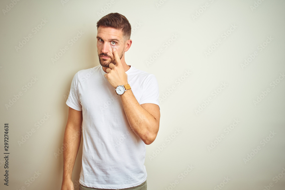 Young handsome man wearing casual white t-shirt over isolated background Pointing to the eye watching you gesture, suspicious expression Young handsome man wearing casual white t-shirt over isolated background Pointing to the eye watching you gesture, suspicious expression