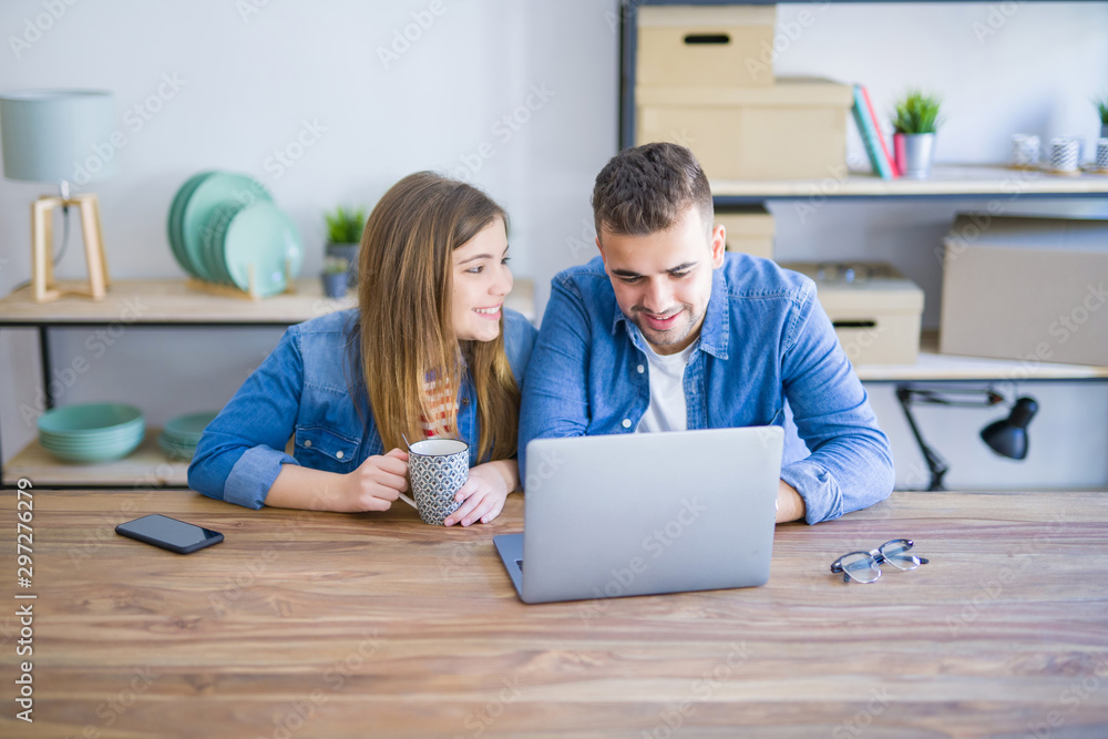 Young couple relaxing drinking a coffee and using the computer laptop around cardboard boxes, very happy moving to a new house Young couple relaxing drinking a coffee and using the computer laptop around cardboard boxes, very happy moving to a new house