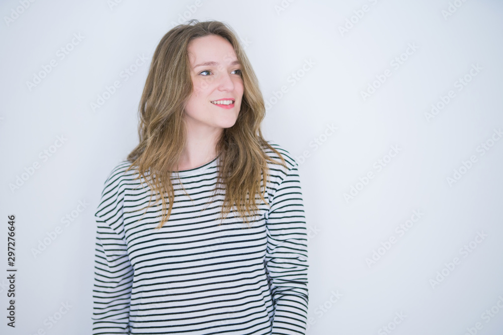Beautiful blonde girl with blue eyes wearing striped sweater over white isolated background looking away to side with smile on face, natural expression. Laughing confident. Beautiful blonde girl with blue eyes wearing striped sweater over white isolated background looking away to side with smile on face, natural expression. Laughing confident.