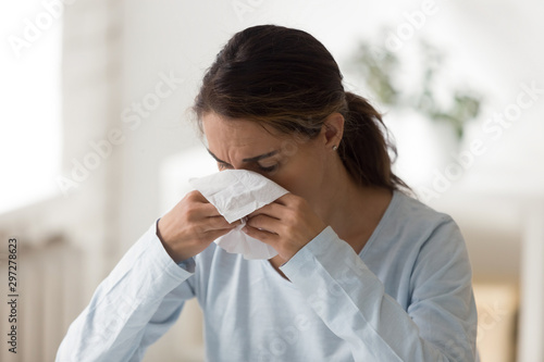 Unhappy millennial lady feeling unwell, wiping runny nose. photo
