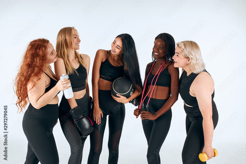 Fototapeta premium Smiling women in black sportive clothes laughing, look at each other, promote healthy lifestyle, people relationship.
