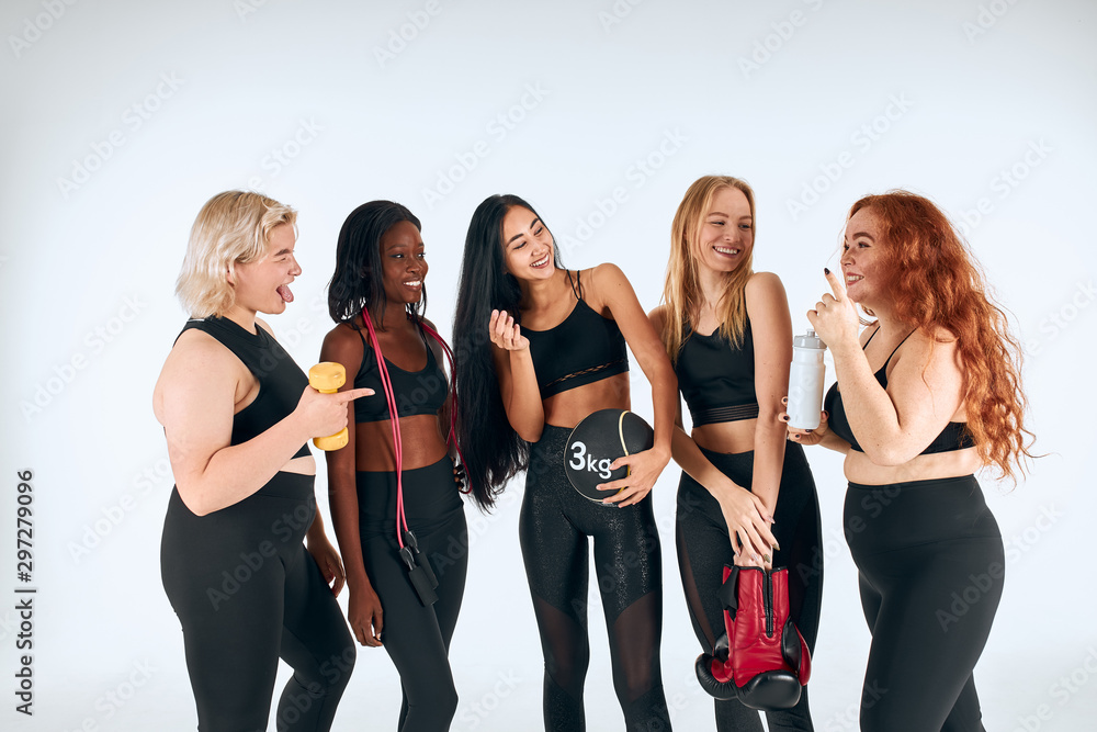 Fototapeta premium Young fitness girls in sportive clothes laughing, look at each other. Portrait og beautiful girls. different nations, sizes, colors. Healthy lifestyle concept